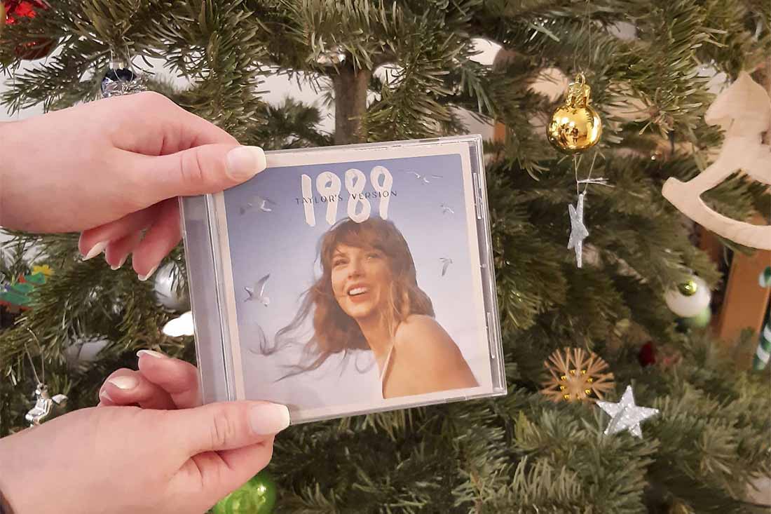 eine Hand hält eine CD von Taylor Swift. Im Hintergrund der geschmückte Weihnachtsbaum