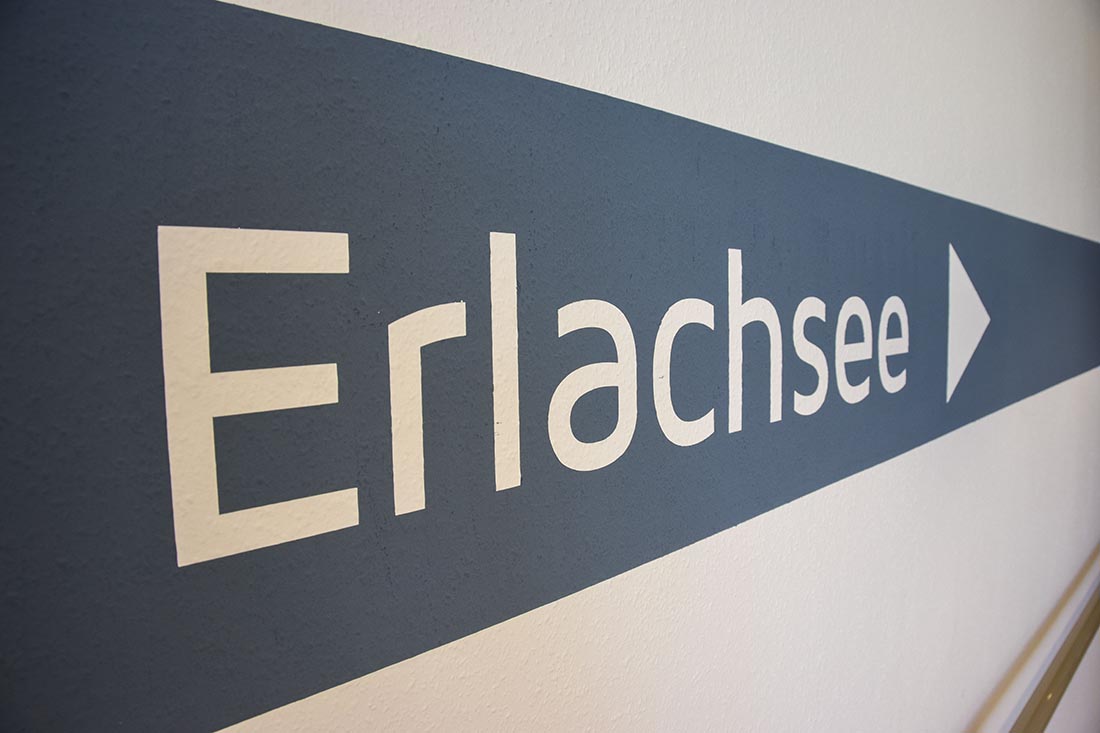 Der Wohngruppennamen Erlachsee ist in weißen Buchstaben auf blauem Hintergrund auf die Wand geschrieben.